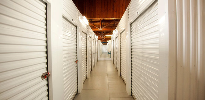 A clean, well lit hallway of indoor storage units with white doors