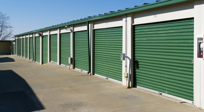 A row of outdoor storage units with green doors in a clean environment