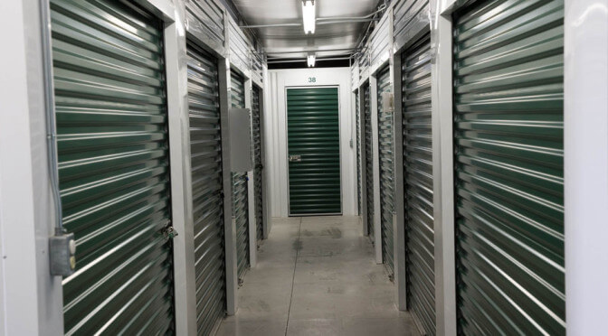 A clean hallway of small indoor storage units with dark green doors