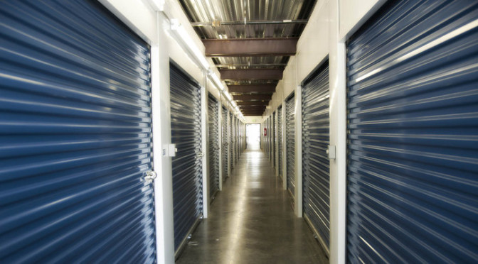 A well lit hallway of indoor storage units with blue doors