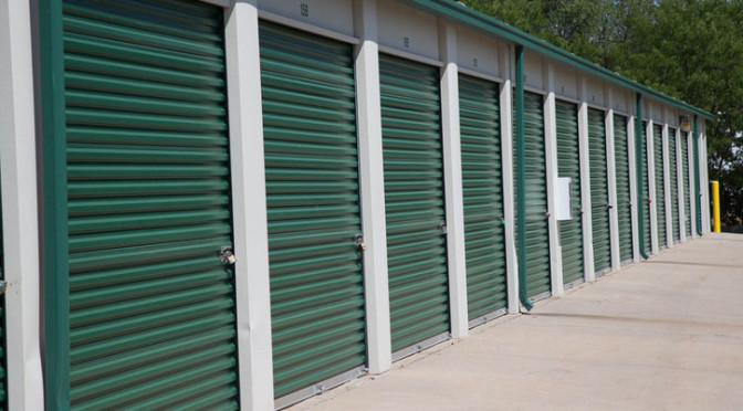 Small outdoor storage units with green doors secured with locks